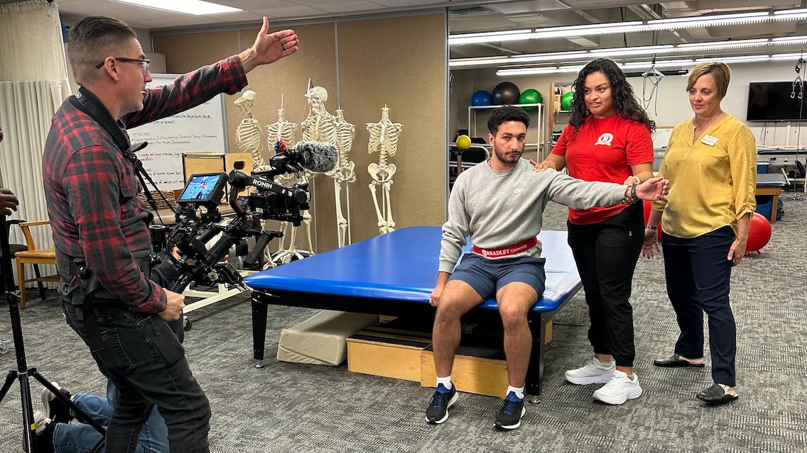 A videographer provides direction to Marissa, a fellow student, and a professor