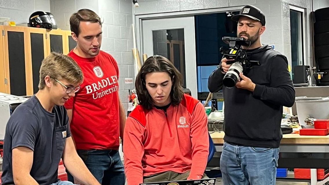 Brandon Johnson stands between two of his friends, with a College Tour videographer recording them from the right